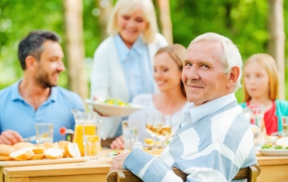 Family having dinner outside, older man looking at camera, blended family, estate planning attorney