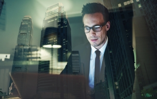 Optimistic businessman working on laptop at office in the night, Working overtime with big city in background