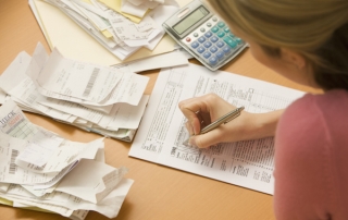 Young woman fills out tax information at her desk with piles of receipts.  Horizontal shot.