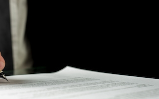 Businessman signing a document or contract in the office, close up horizontal banner format of his hand and the paperwork with copyspace.